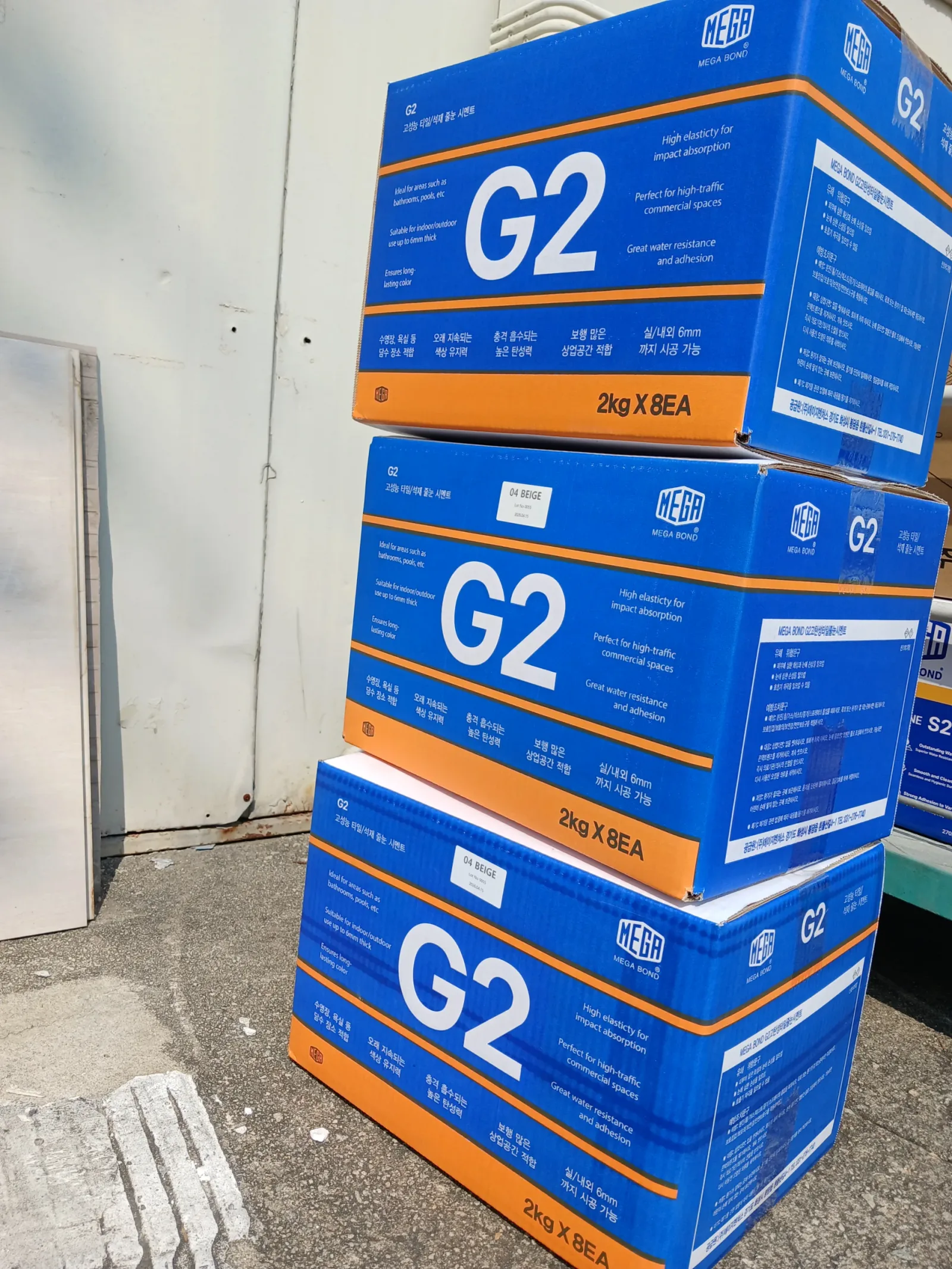 MEGA G2 줄눈시멘트 박스가 야외 창고 앞에 층층이 쌓여 있는 모습